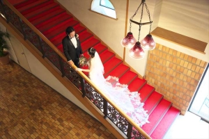 千里阪急ホテルにて赤階段の手すりを持って向かい合う新郎新婦