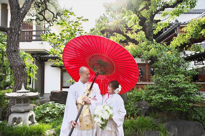結婚式持ち込みカメラマンが撮影：お寺の庭で番傘を持ちながらお互いに微笑む新郎新婦